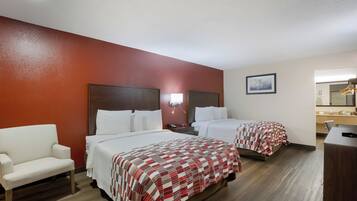 A hotel room with two beds, a chair, a desk, and a mirror.