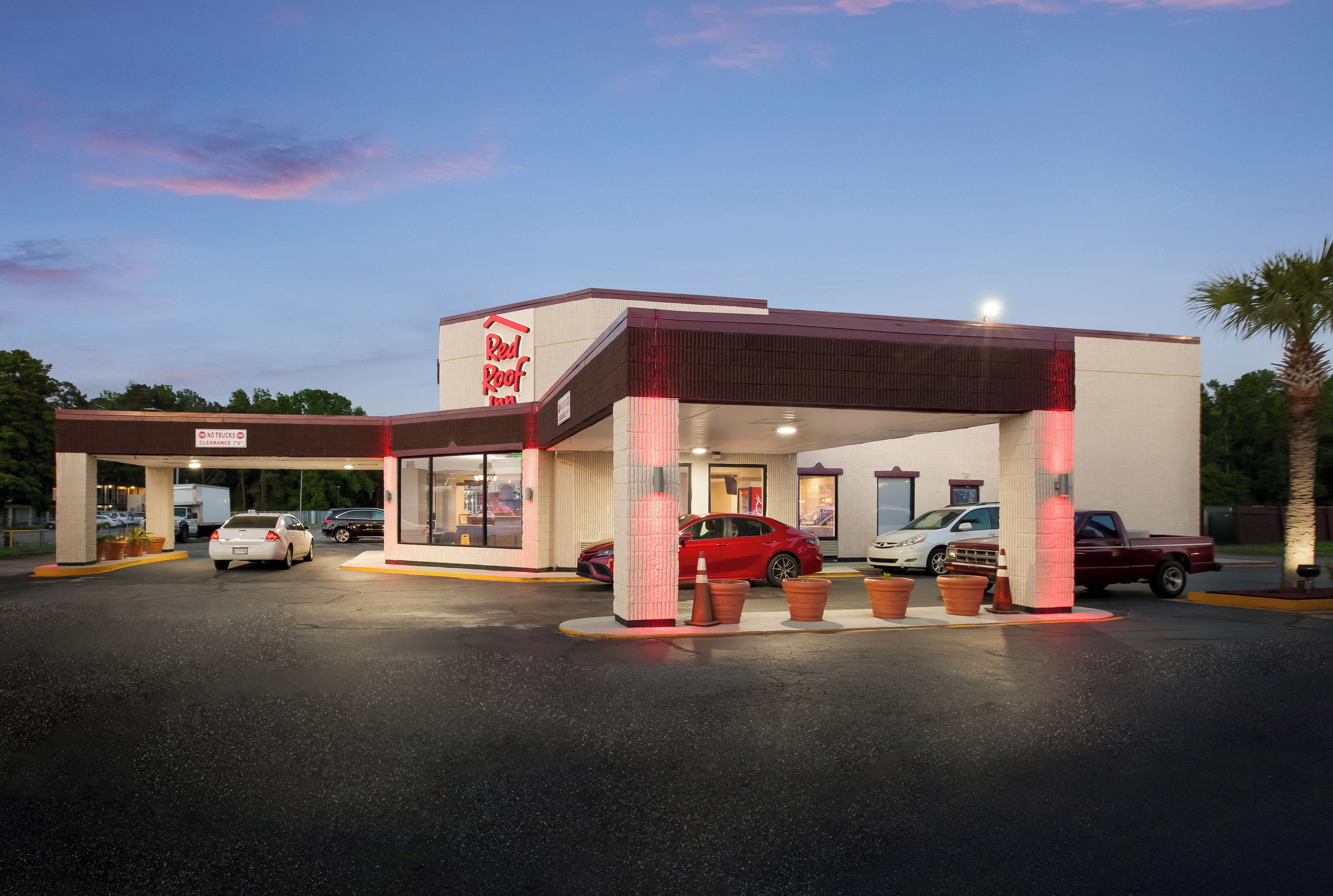 A Red Roof Inn with a covered parking area, multiple cars parked, and a clear sky in the background.