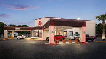 A Red Roof Inn with a covered parking area, multiple cars parked, and a clear sky in the background.