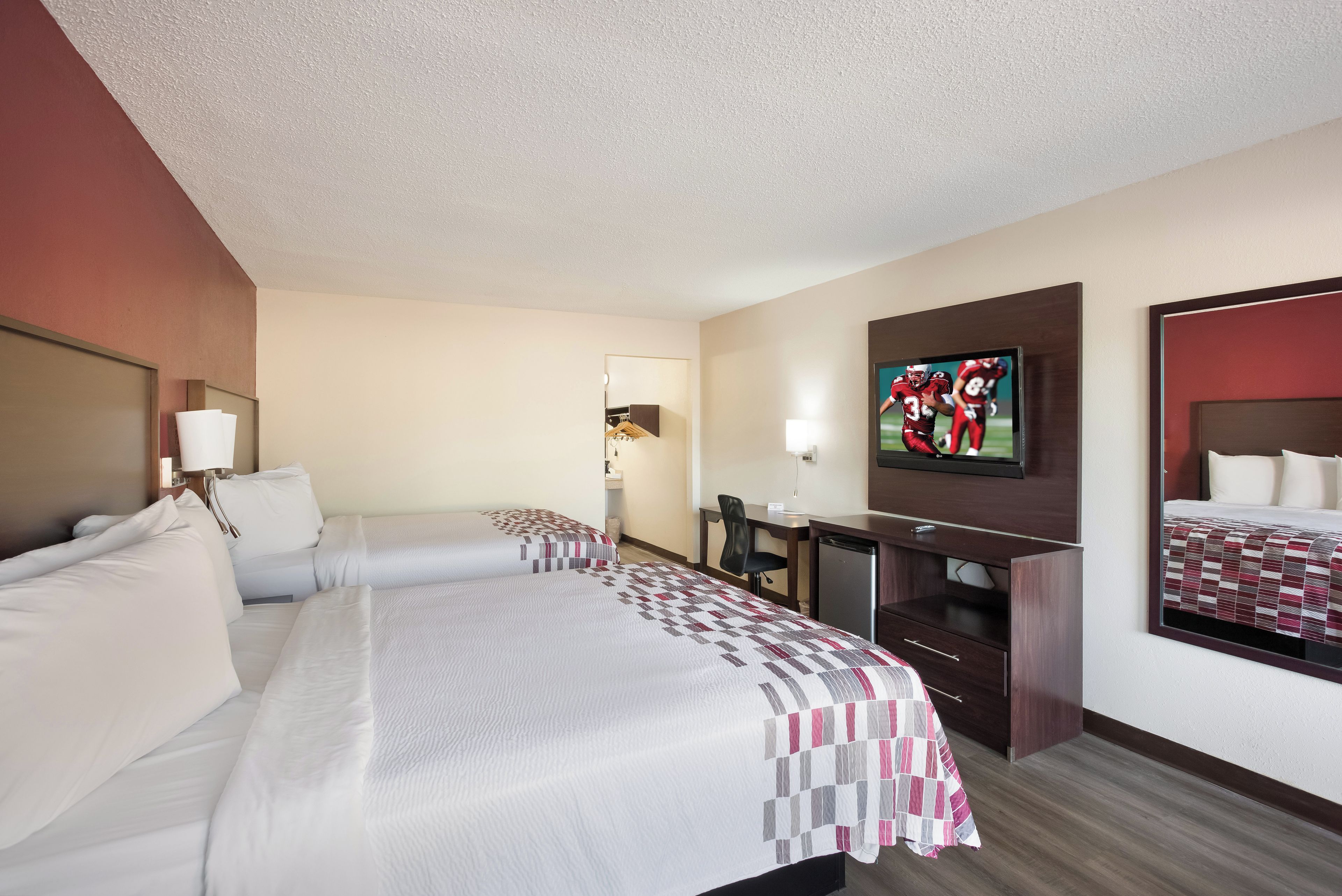 A hotel room with two beds, a desk, a television, and a mirror.
