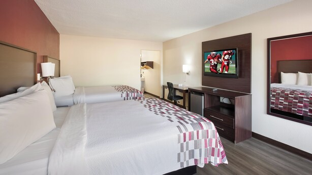 A hotel room with two beds, a desk, a television, and a mirror.