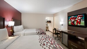 A hotel room with two beds, a desk, a television, and a small refrigerator.