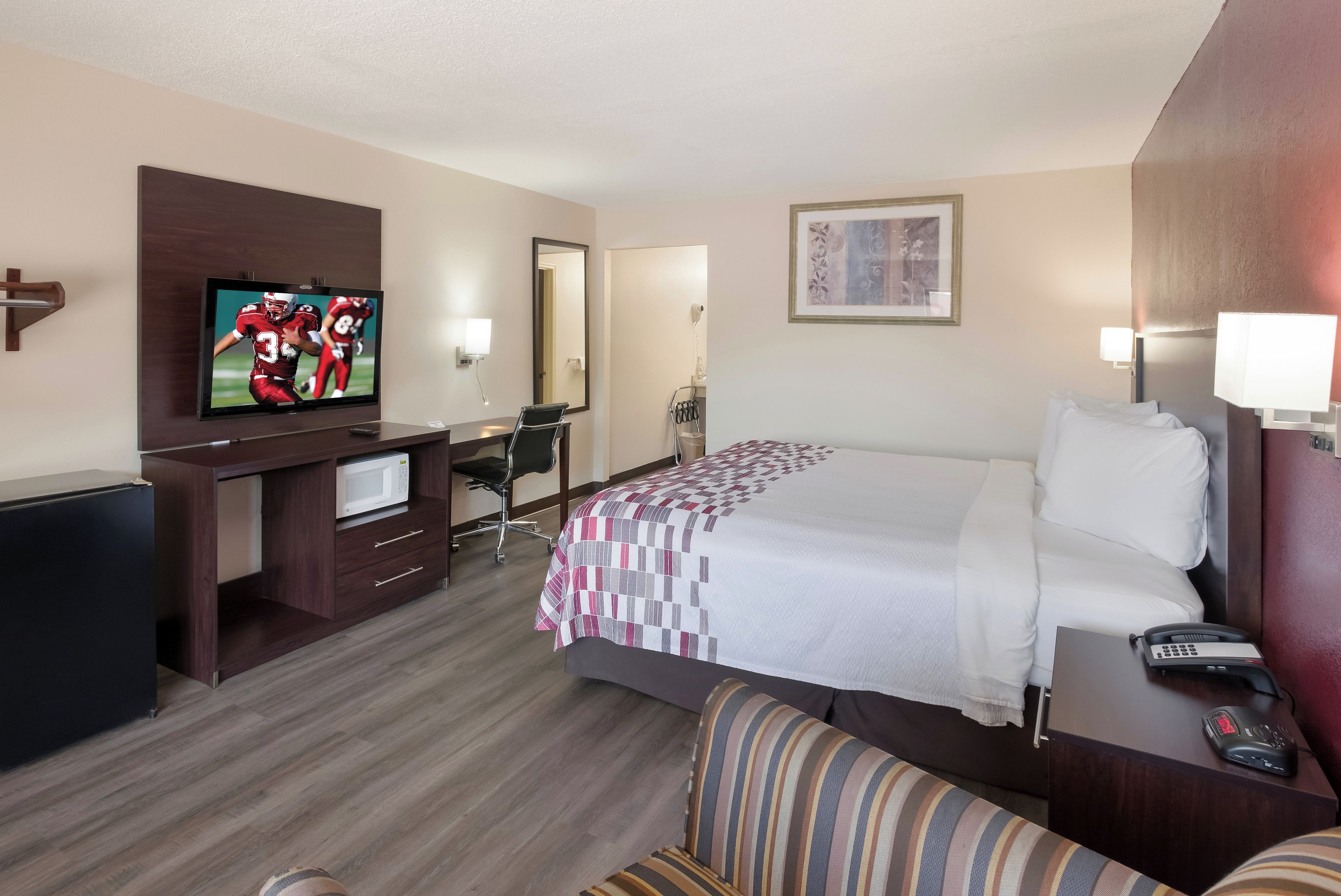 A hotel room with a bed, a TV, a desk with a chair, a bedside table with a lamp, and a telephone.