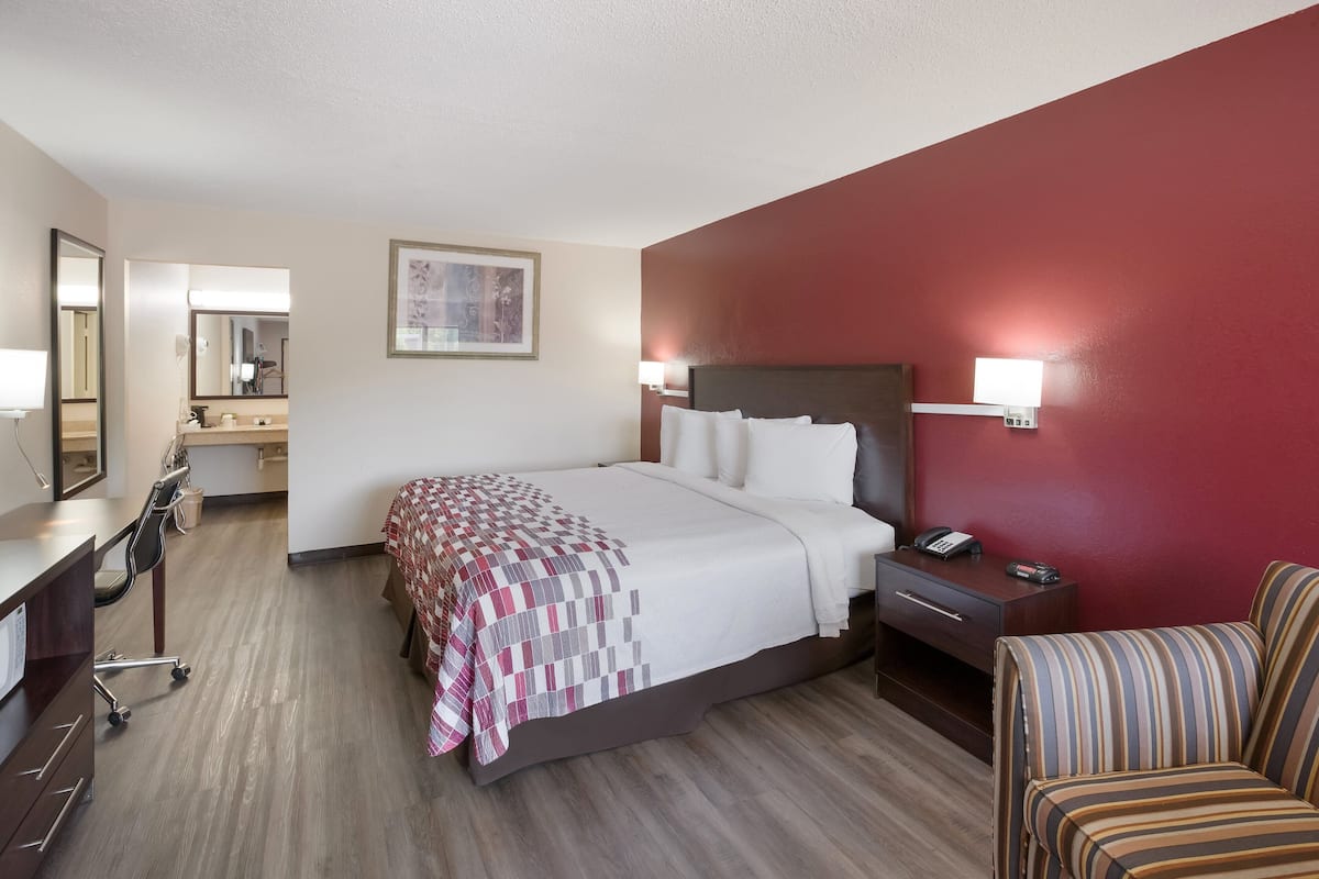 A hotel room with a bed, bedside table, chair, desk, and a mirror.