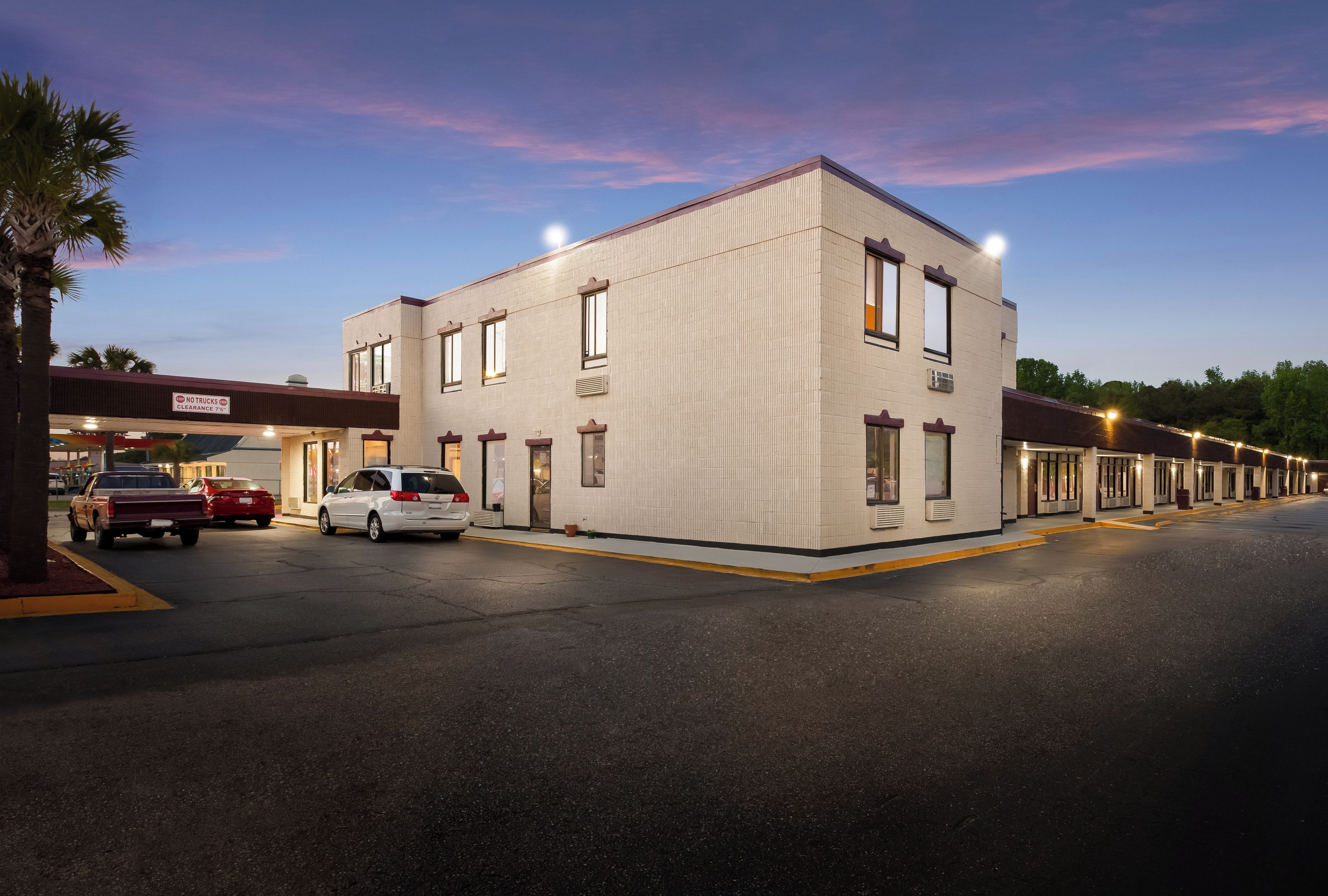 A motel with a single-story building, a parking lot, and a row of rooms.