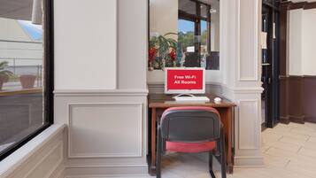 Habitación de hotel con escritorio, silla y un cartel que indica Wi-Fi gratuito en todas las habitaciones.