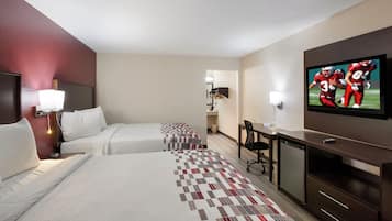 Habitación de hotel con dos camas, un escritorio, una televisión y una nevera pequeña.