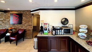 A kitchen area with a coffee machine, toaster, microwave, and a sign that says 'I NEED COFFEE.'