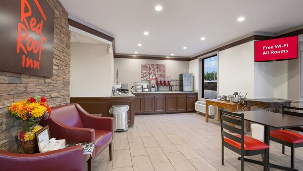 A Red Roof Inn reception area with a stone wall, a vase of flowers, a desk, and a sign indicating free Wi-Fi in all rooms.