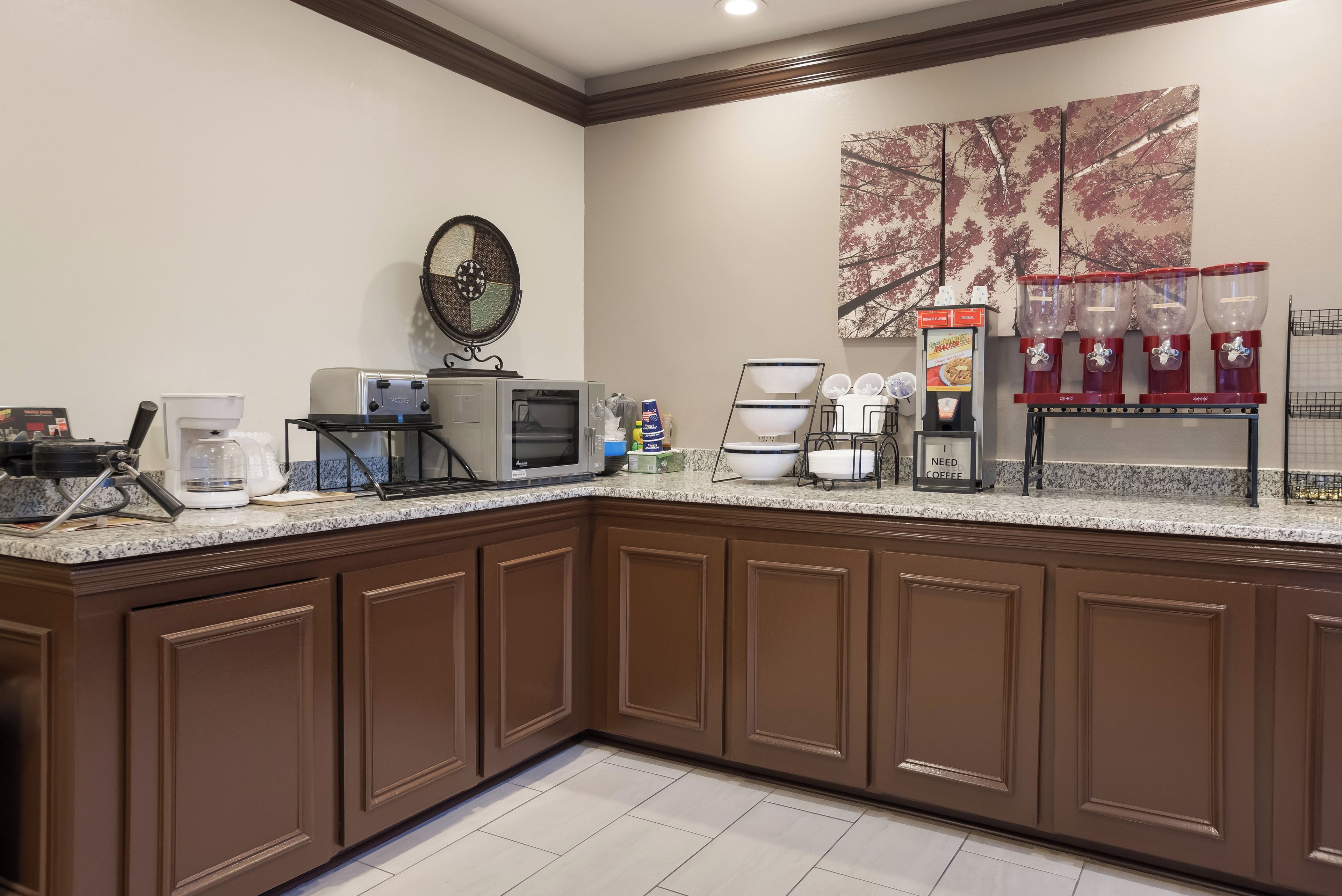 A hotel kitchen with a coffee station, microwave, toaster, and a large decorative wall piece.