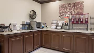 A hotel kitchen with a coffee station, microwave, toaster, and a large decorative wall piece.
