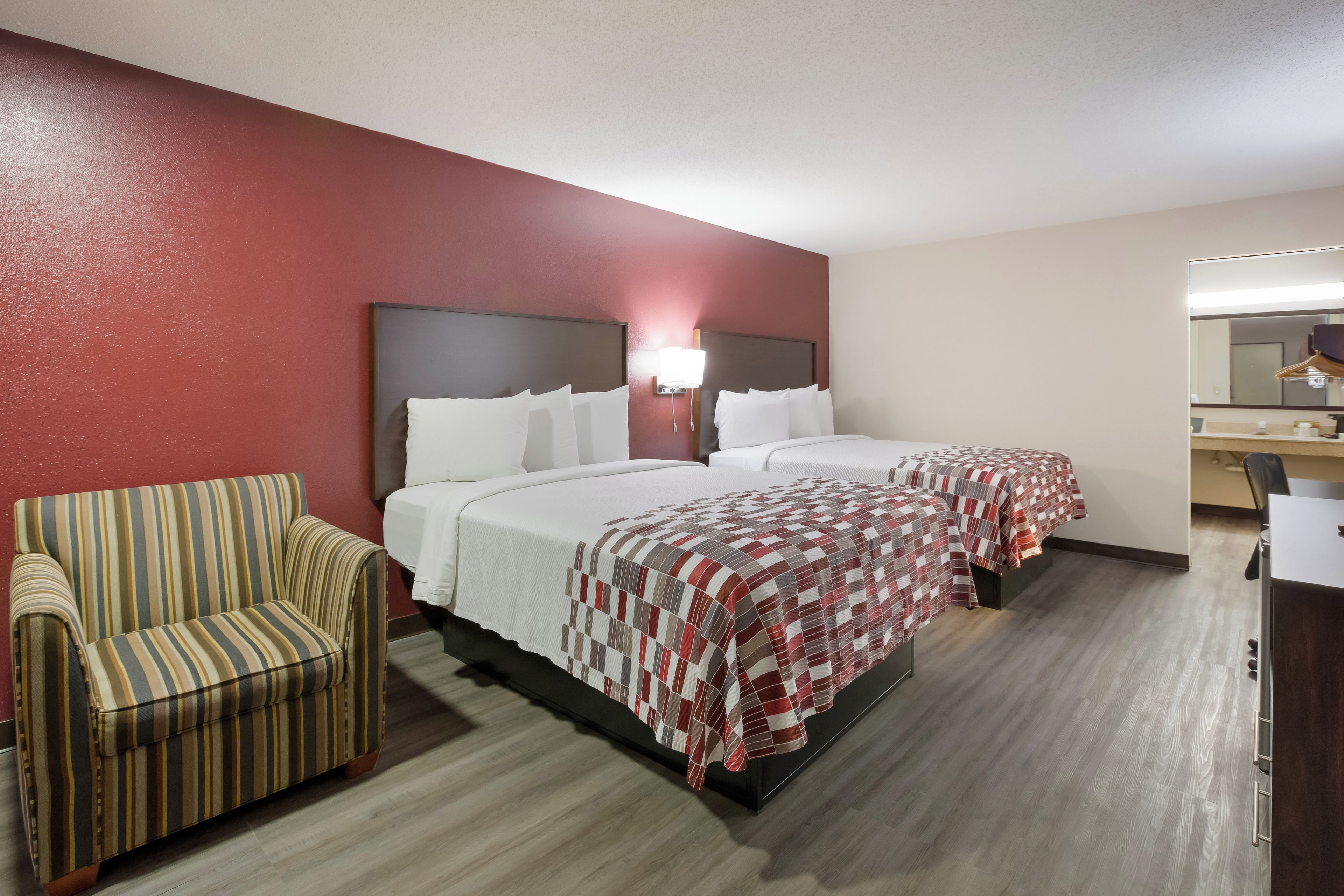 A hotel room with two beds, a striped armchair, a desk, and a mirror.