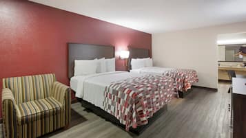 A hotel room with two beds, a striped armchair, a desk, and a mirror.