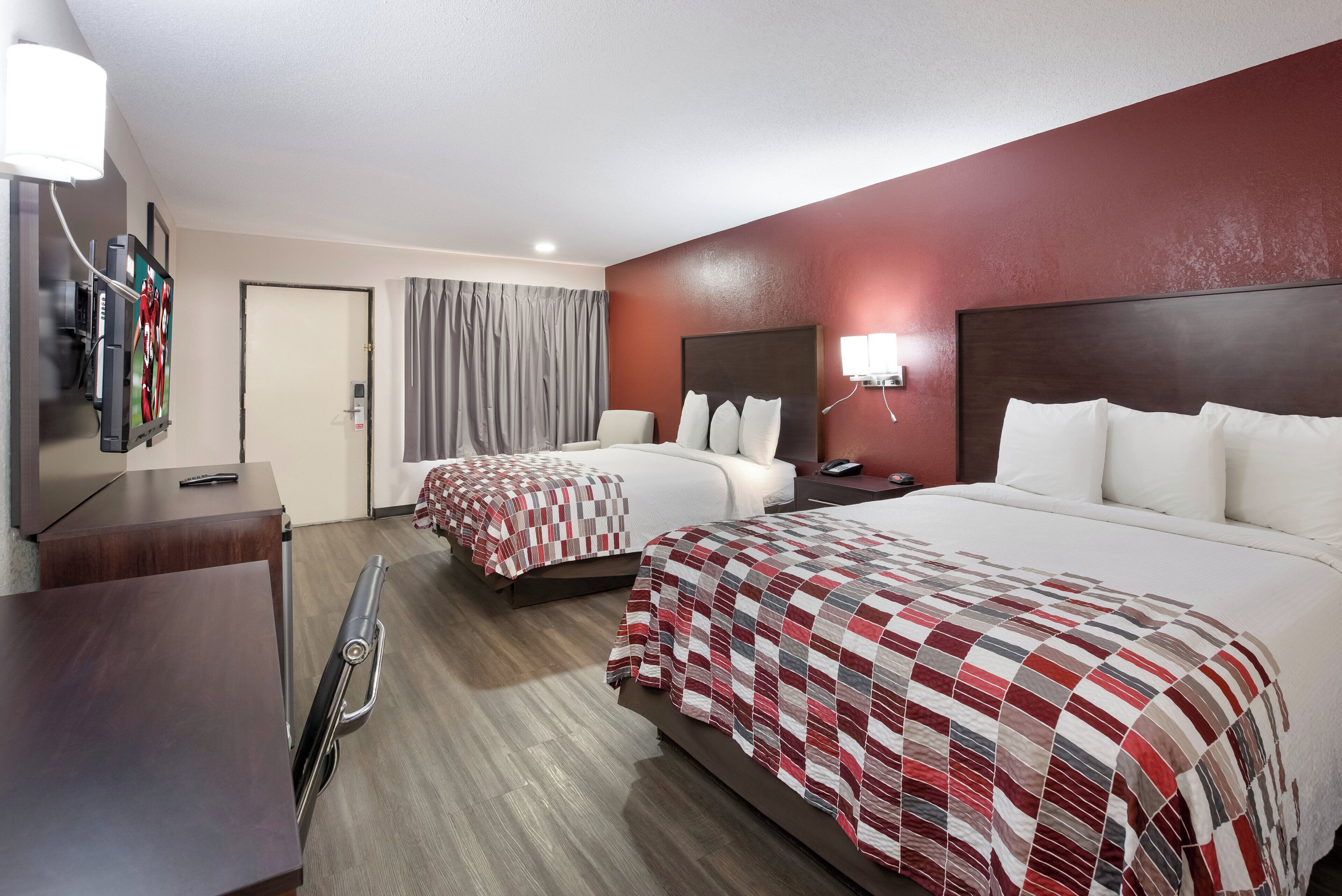 A hotel room with two beds, a desk with a chair, a TV, and a bathroom.