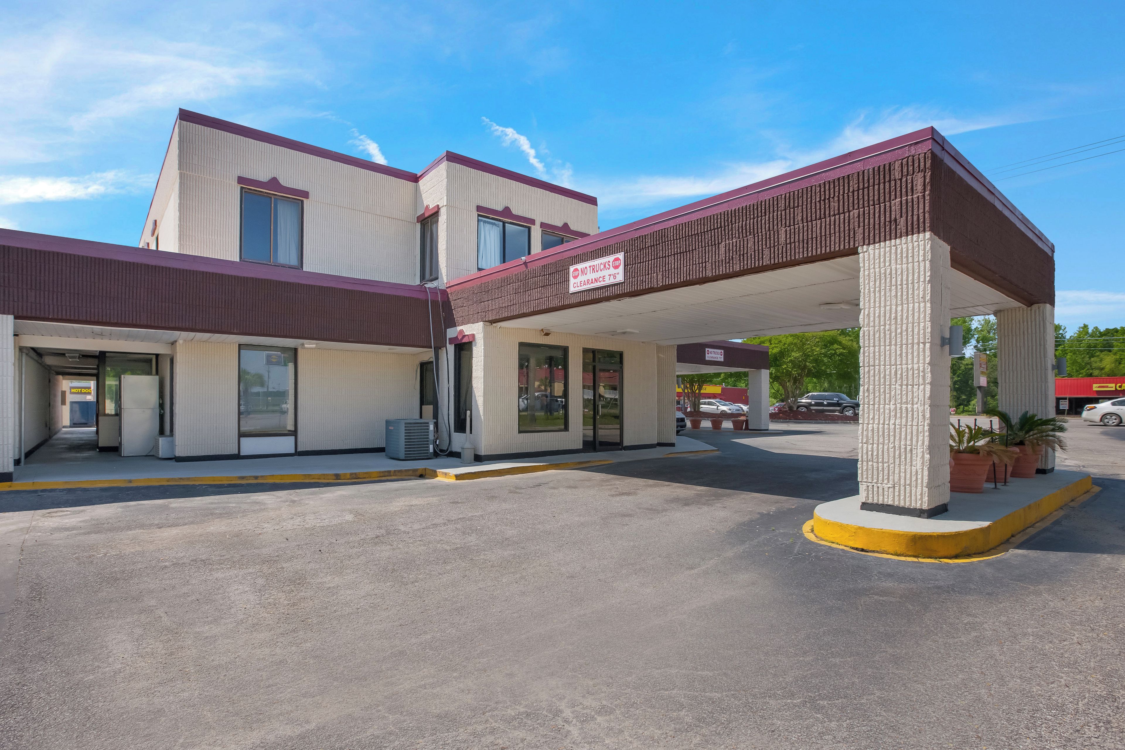 A motel with a covered parking area, a 'No Trucks Stop' sign, and a 'Clearance 7'6'' sign.