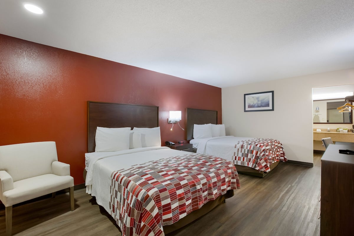 A hotel room with two beds, a sofa, a desk, and a mirror.