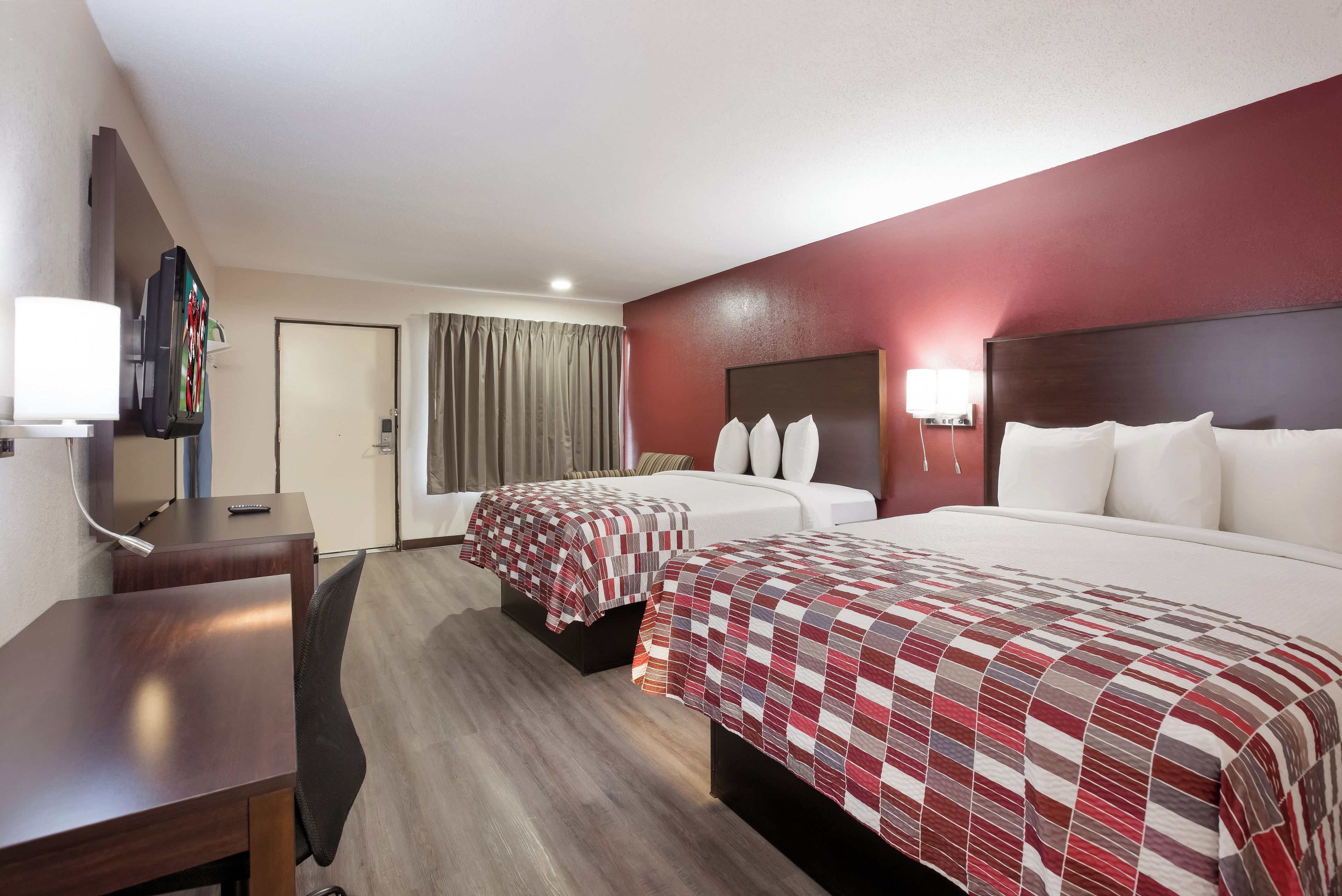 Habitación de hotel con dos camas, un escritorio, televisor y puerta de baño.