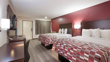 Habitación de hotel con dos camas, un escritorio, televisor y puerta de baño.