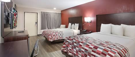 A hotel room with two beds, a desk, a TV, and a bathroom.