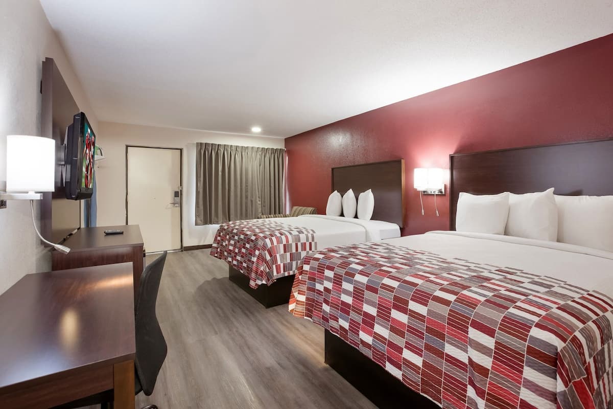 A hotel room with two beds, a desk, a TV, and a window with curtains.