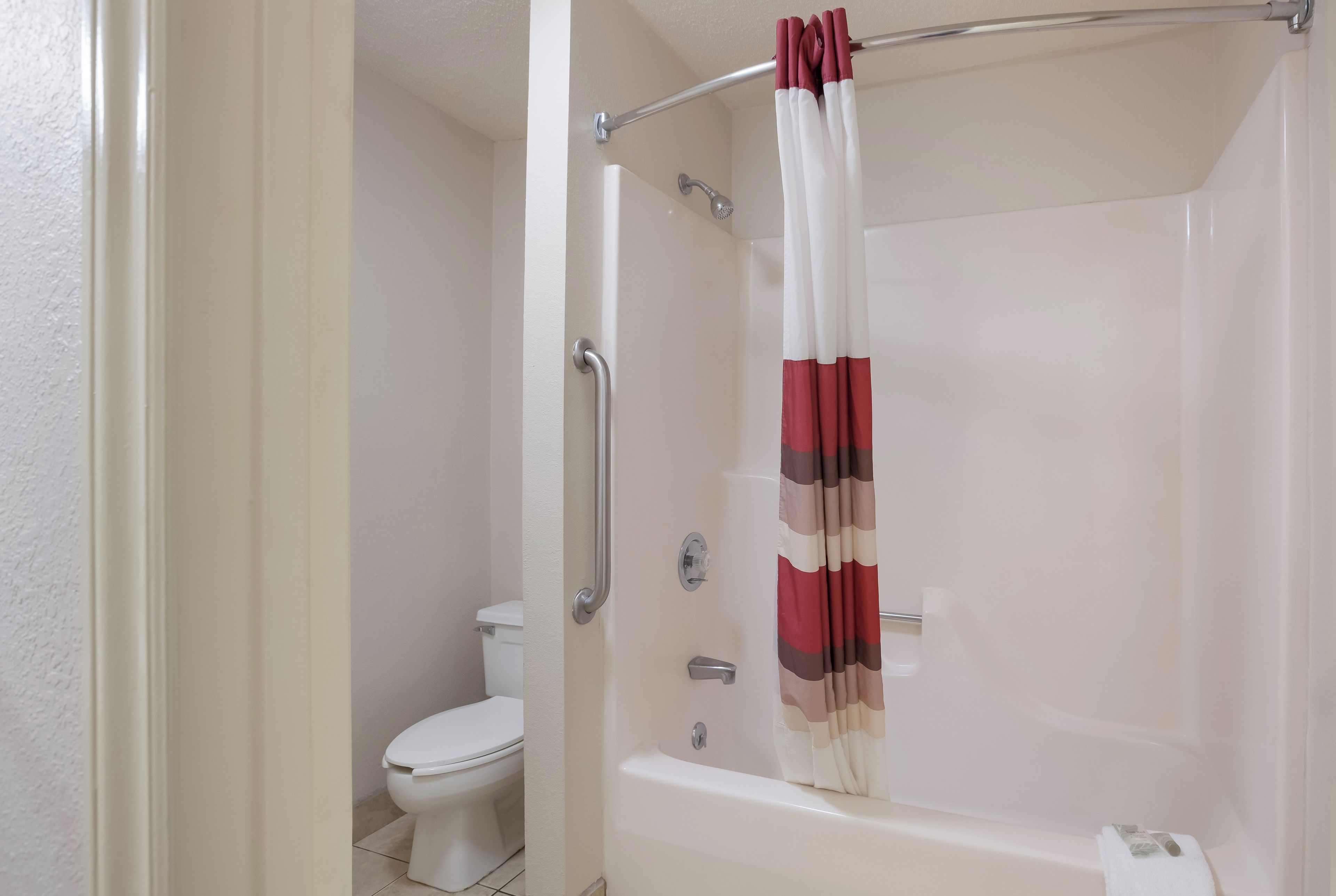 Un baño con una bañera blanca, una ducha con barra de apoyo de metal y un inodoro.