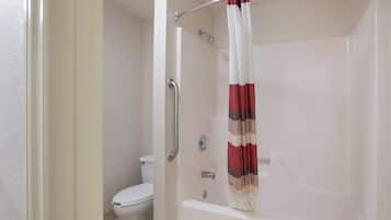 Un baño con una bañera blanca, una ducha con barra de apoyo de metal y un inodoro.