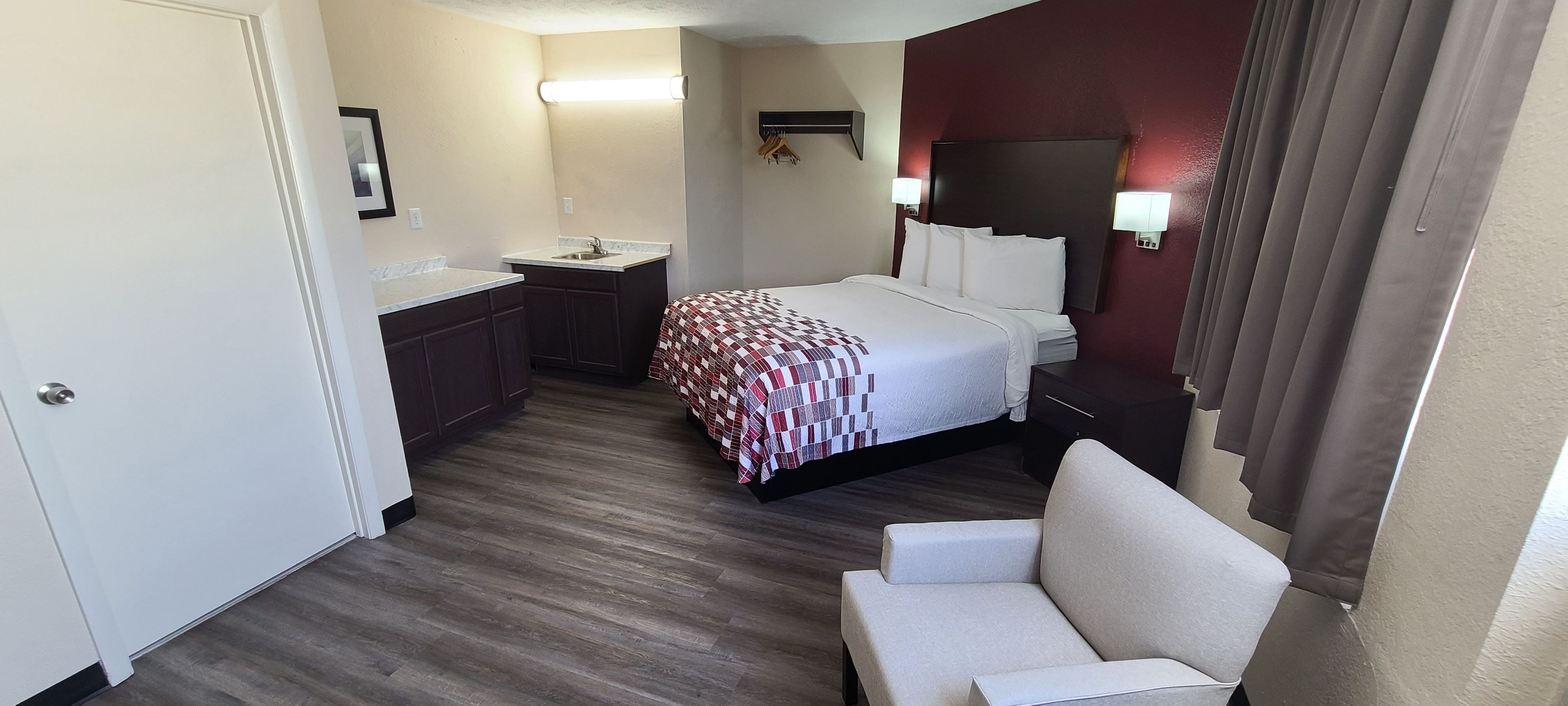 A hotel room with a bed, a small desk with a sink, a chair, and a mirror.
