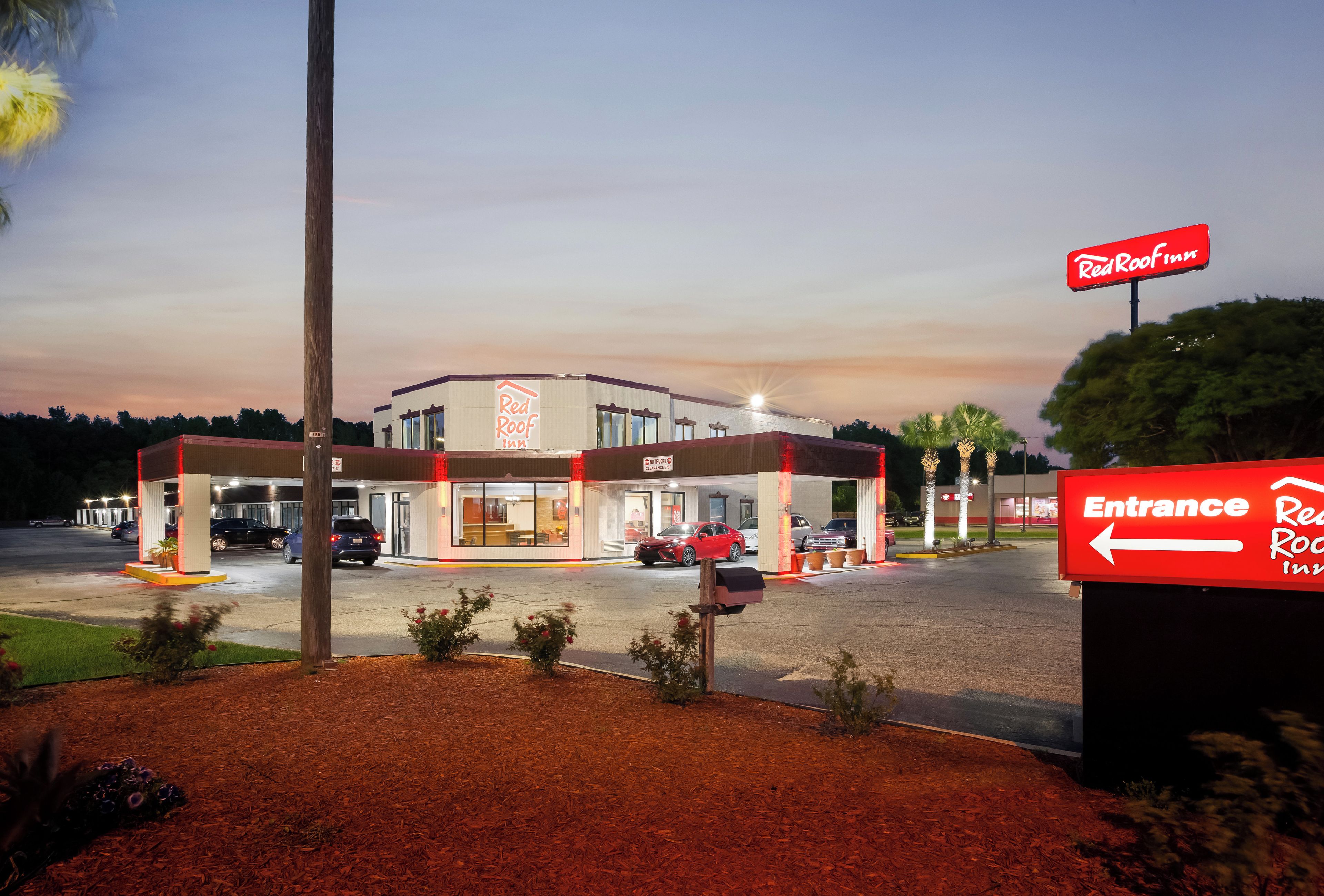 A Red Roof Inn with a clear entrance sign, a parking lot with several cars, and a well-lit building facade.