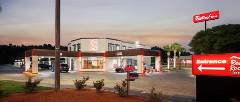 Un hôtel Red Roof Inn avec une enseigne d’entrée bien visible, un parking avec plusieurs voitures et une façade d’immeuble bien éclairée.