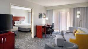 A hotel room with a bed, a desk, a television, a sofa, and a red cabinet. - Courtyard by Marriott Macon (Macon)
