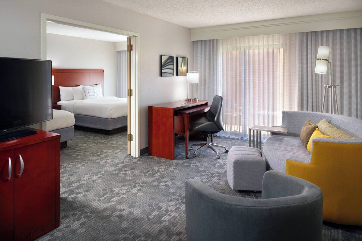 A hotel room with a bed, a desk, a television, a sofa, and a red cabinet.