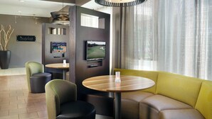 A modern hotel lobby with a seating area, a television, and a sign indicating a market. - Courtyard by Marriott Macon (Macon)