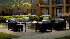 An outdoor seating area with a stone fire pit, surrounded by wicker furniture and a well-maintained lawn. - Courtyard by Marriott Macon (Macon)