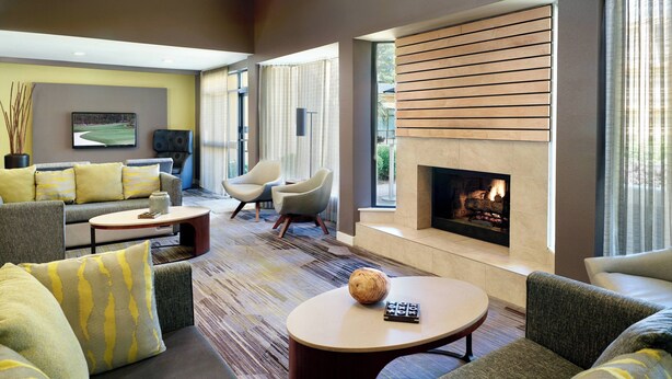 A modern living room with a fireplace, comfortable seating, and a large window. - Courtyard by Marriott Macon (Macon)