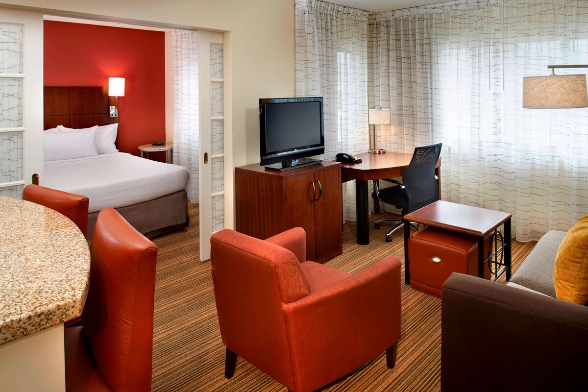 A hotel room with a bed, a desk, a chair, a television, and a lamp.