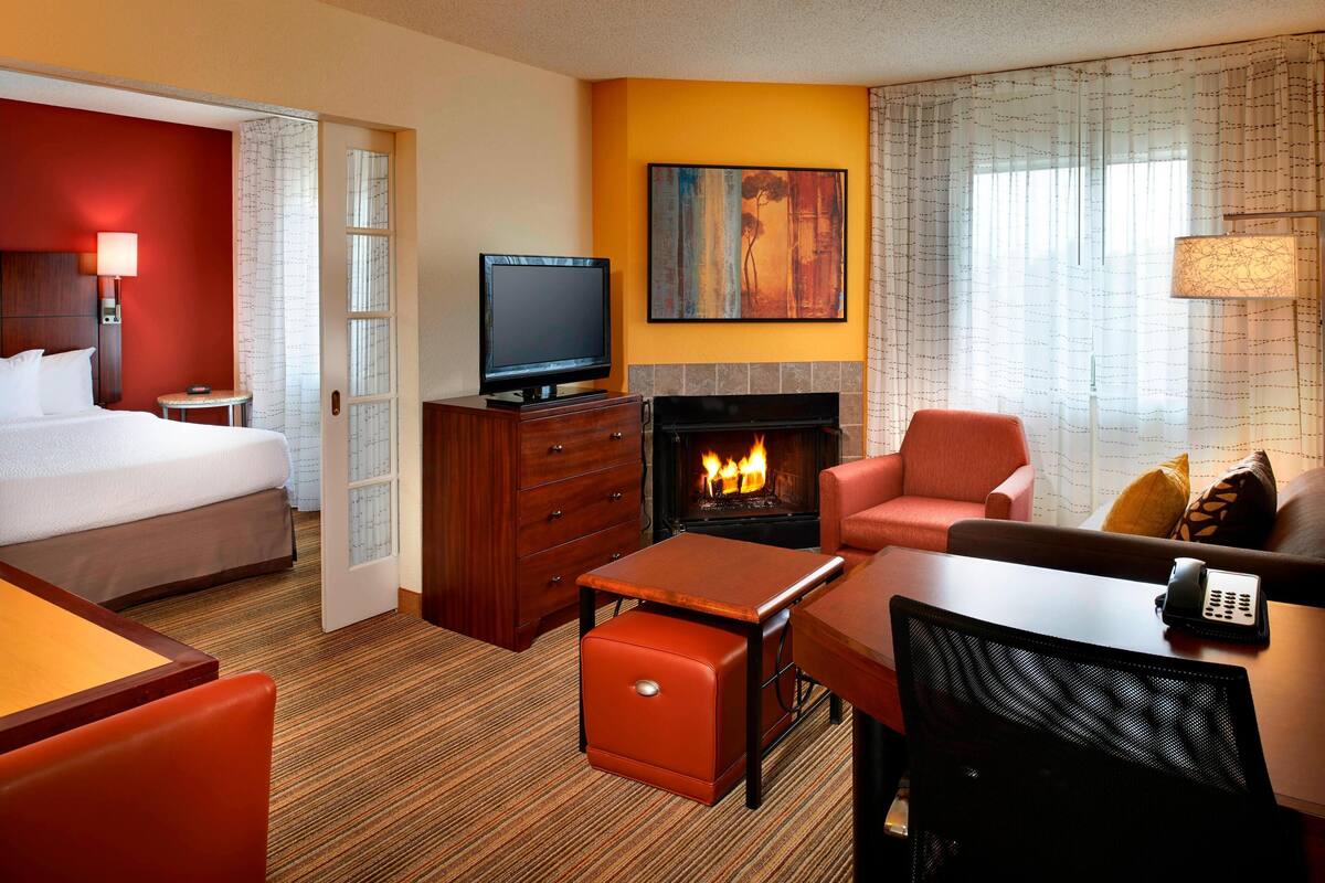 A hotel room with a bed, a TV, a fireplace, a sofa, and a desk.