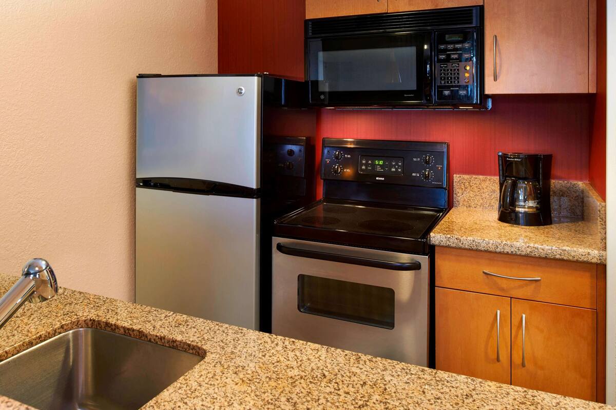 A kitchen with a stainless steel refrigerator, a microwave, an oven, and a coffee maker on the countertop.