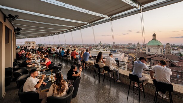 An outdoor dining area with tables and chairs, overlooking a cityscape with a prominent green dome building. - Hotel Dei Cavalieri Milano Duomo (Milan)