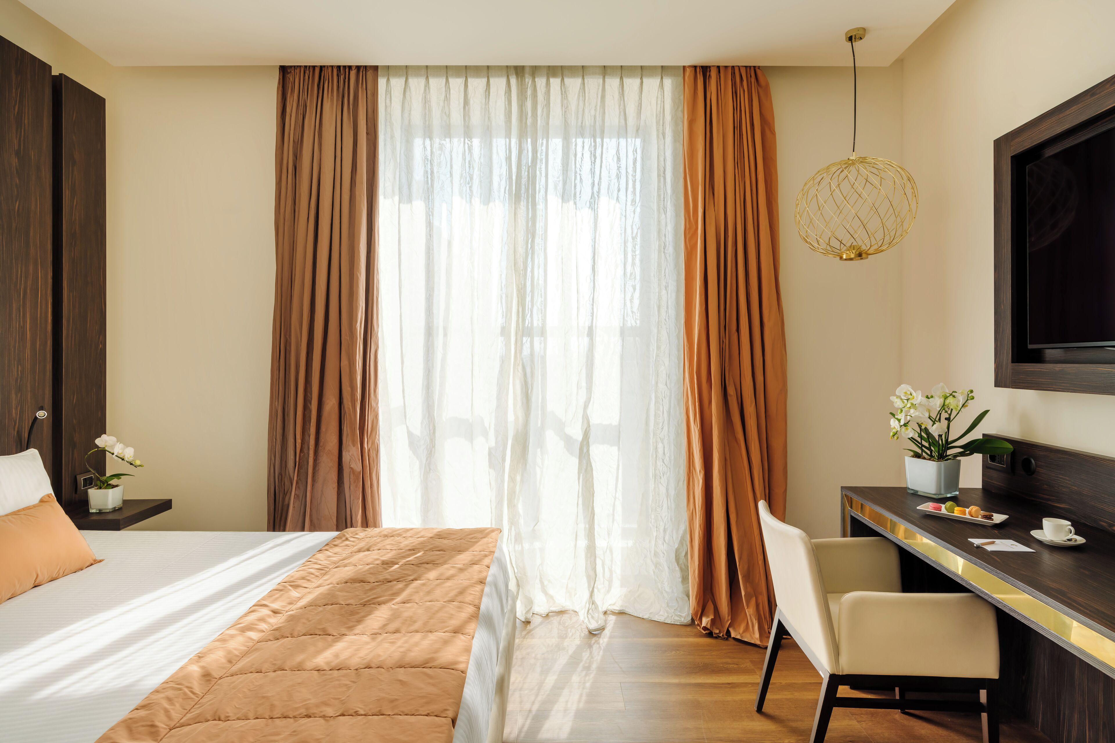 A hotel room with a large bed, a desk with a chair, a television, and a window with curtains.