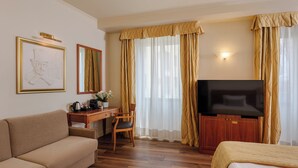 A hotel room with a sofa, a desk with a chair, a television, and curtains. - Hotel Dei Cavalieri Milano Duomo (Milan)