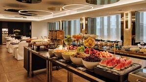 A buffet with various fruits and dishes, a modern ceiling design, and a view of the city through large windows. - Hotel Dei Cavalieri Milano Duomo (Milan)