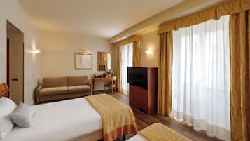 Une chambre d’hôtel avec deux lits, un canapé, un bureau avec une télévision et de grandes fenêtres avec des rideaux.