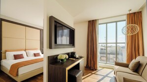A hotel room with a bed, a TV mounted on the wall, a seating area with a sofa, and a large window with curtains. - Hotel Dei Cavalieri Milano Duomo (Milan)
