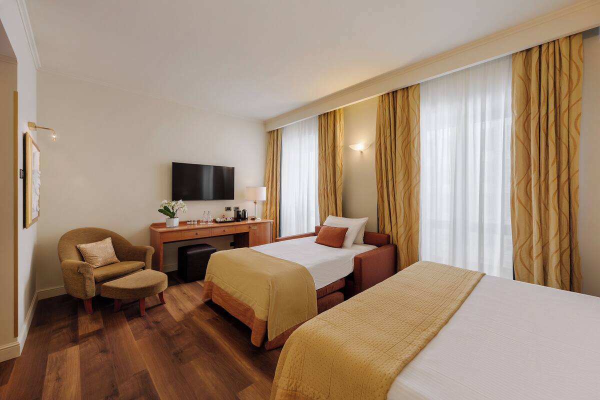 Habitación de hotel con dos camas, un escritorio, una silla y un televisor.