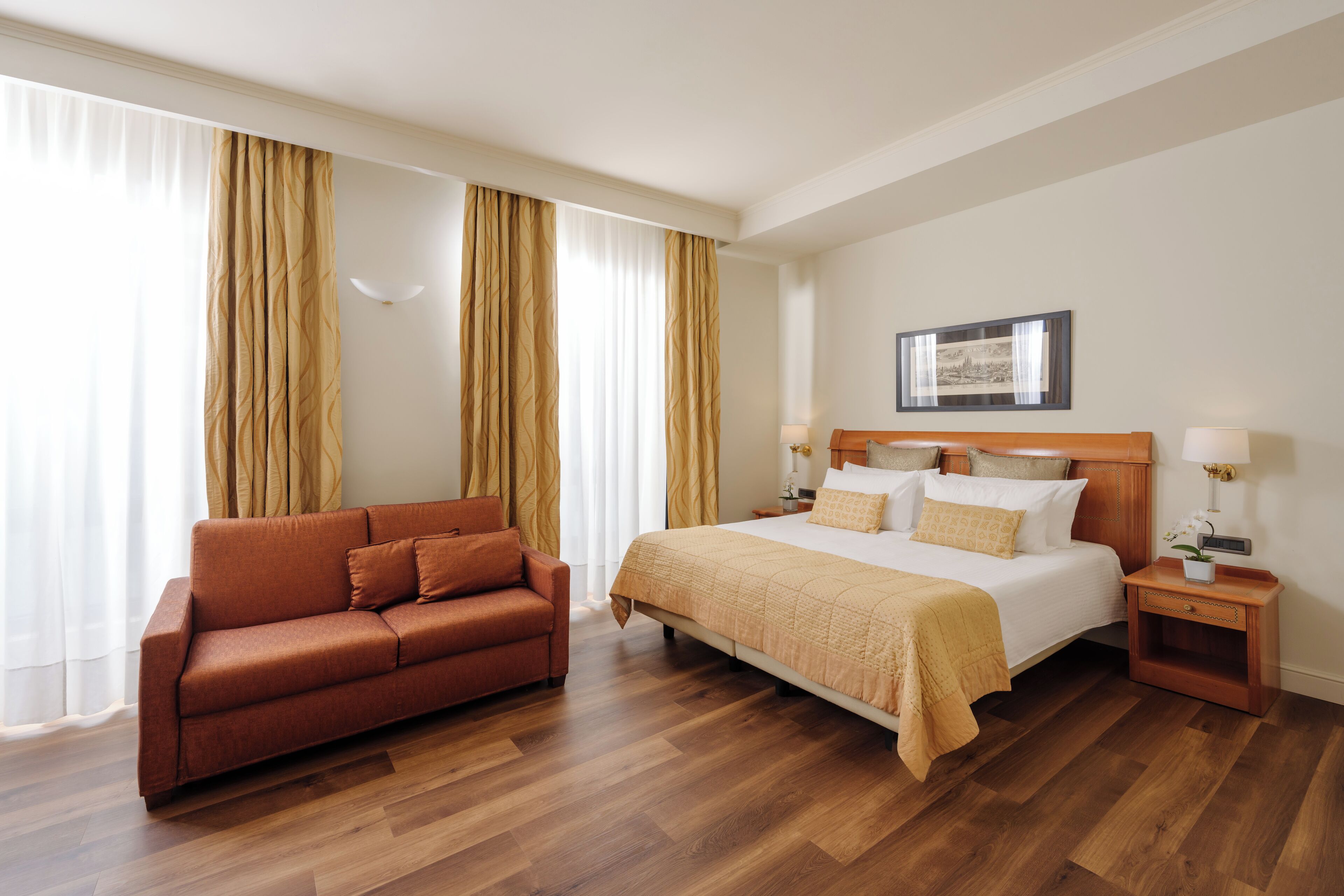 Une chambre d’hôtel avec un lit, un canapé, un plancher en bois et des rideaux.