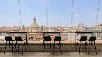 Una terrazza con tavoli e sedie affacciata su una vista urbana che comprende edifici storici e grattacieli moderni.