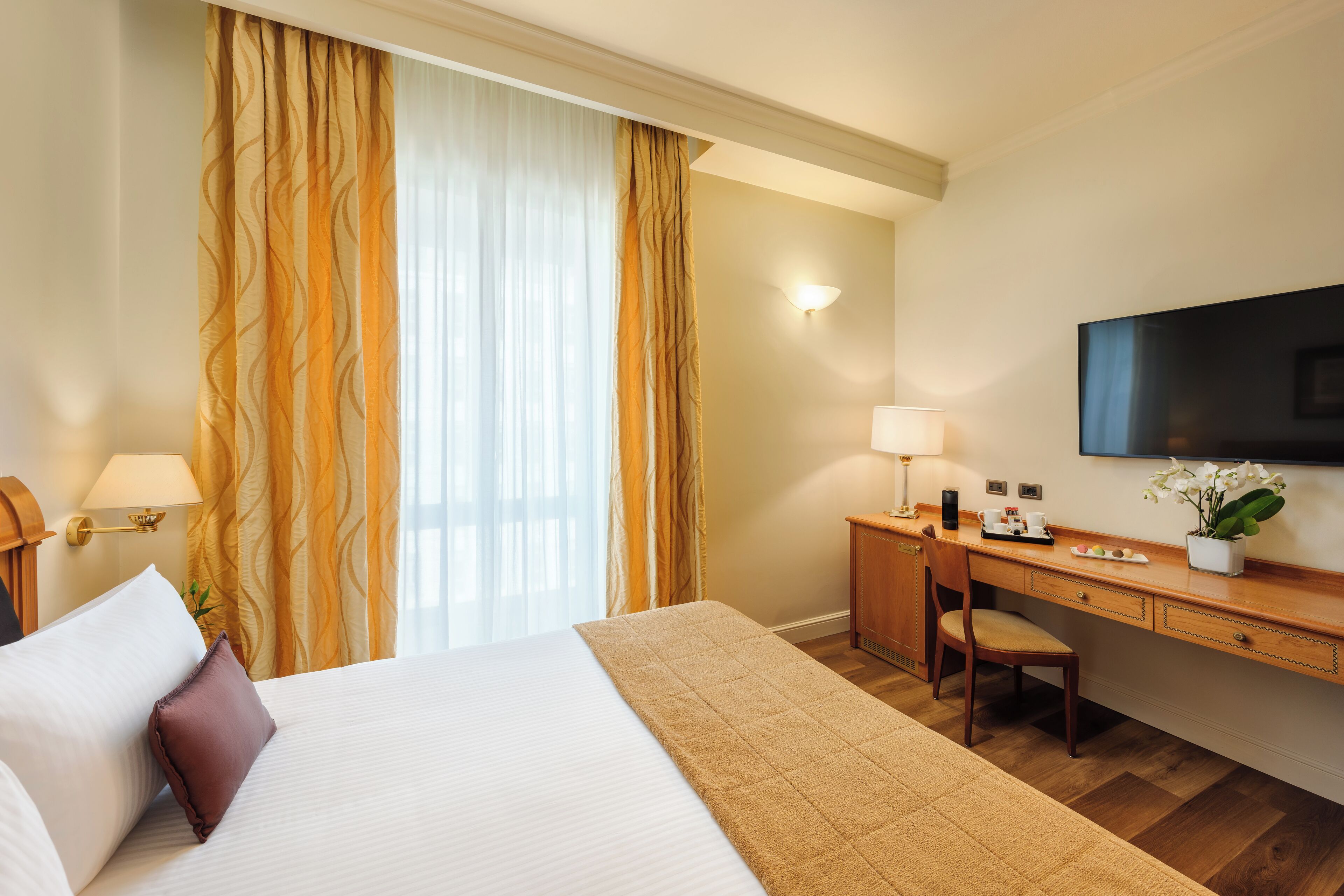 A hotel room with a bed, a desk, a chair, a TV, and a window with curtains.