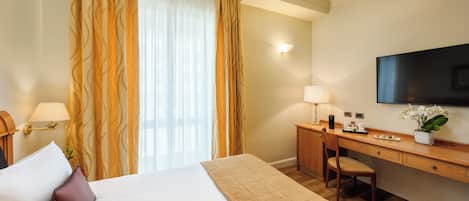 Habitación de hotel con cama, escritorio, silla, televisor y ventana con cortinas.