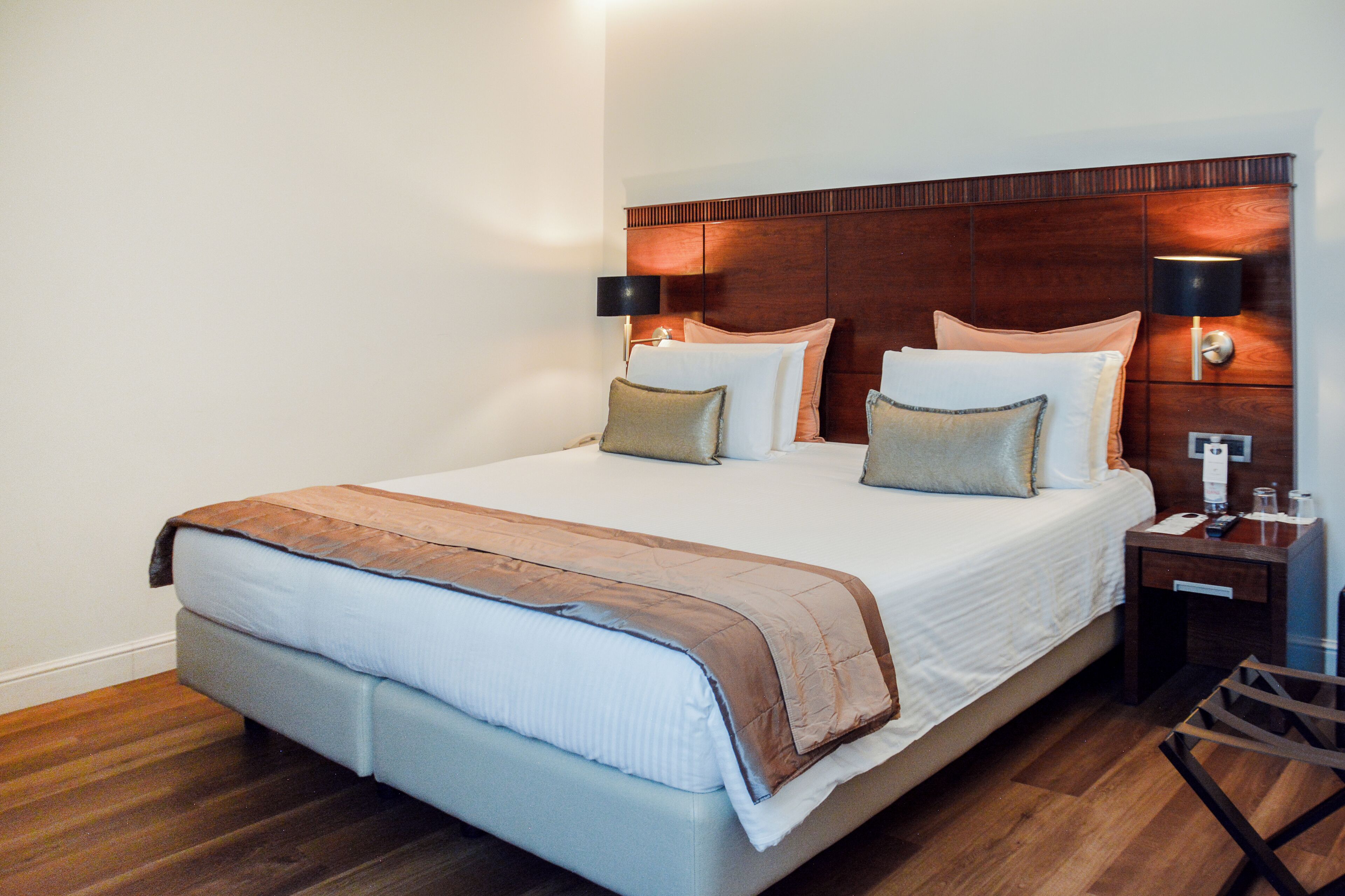 A hotel room with a large bed, two bedside tables, a wooden headboard, and a nightstand with a lamp.