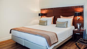 Hotelkamer met een groot bed, twee nachtkastjes, een houten hoofdbord en een bijzettafeltje met een lamp.